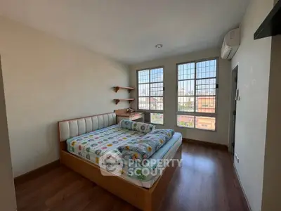 Cozy bedroom with large windows and wooden flooring, featuring a comfortable bed and air conditioning.