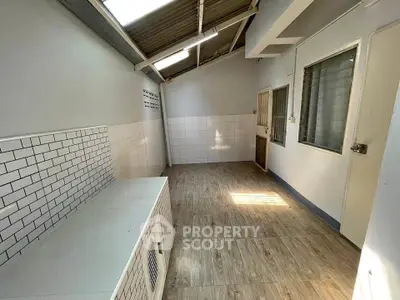 Spacious utility room with tiled walls and wooden flooring, ideal for storage or laundry setup.