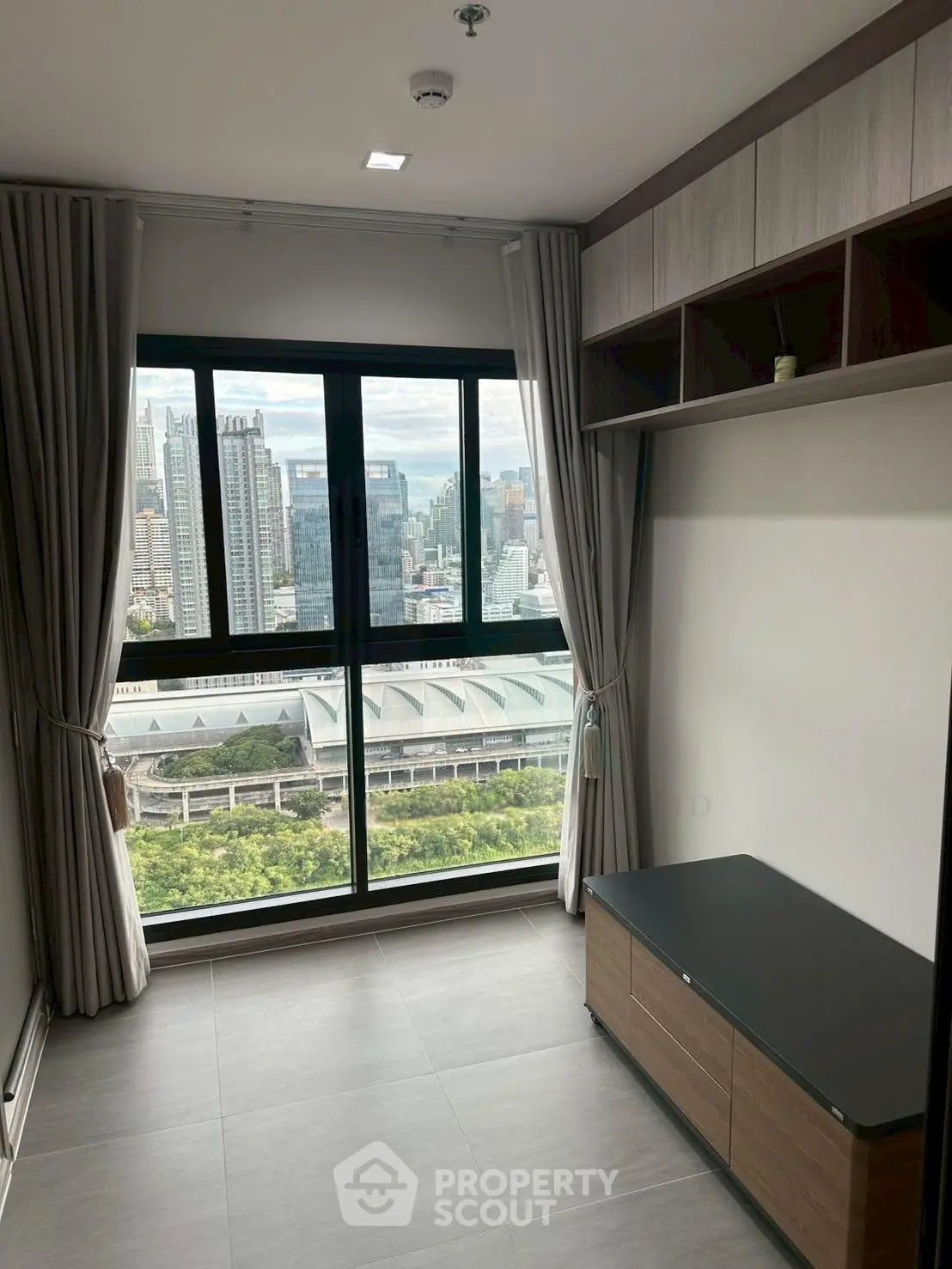 Modern apartment with large window offering stunning cityscape view, sleek storage, and elegant curtains.