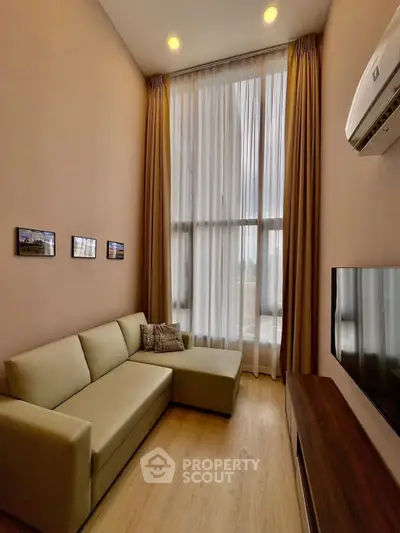 Modern living room with high ceiling and large window, featuring a comfortable sofa and wall-mounted TV.