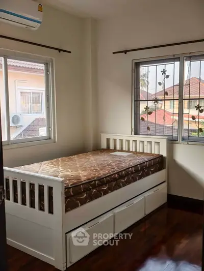 Cozy bedroom with single bed and wooden flooring, bright natural light from windows.