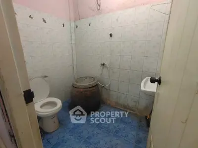 Basic bathroom with blue tile flooring and a traditional water storage barrel.