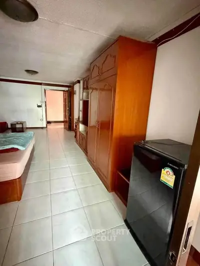 Cozy bedroom with wooden wardrobe and compact fridge, ideal for urban living.