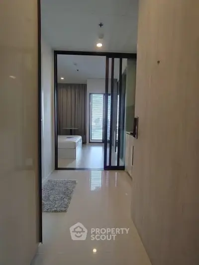 Modern apartment hallway leading to a bright bedroom with large windows and sleek design.