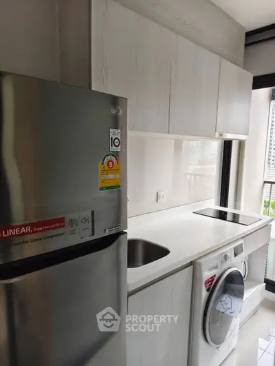 Modern kitchen with sleek appliances and city view, featuring fridge and washing machine.