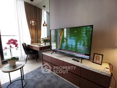 Modern living room with large TV, stylish decor, and natural light from floor-to-ceiling windows.