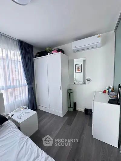 Modern bedroom with sleek white furniture and air conditioning, featuring large windows for natural light.