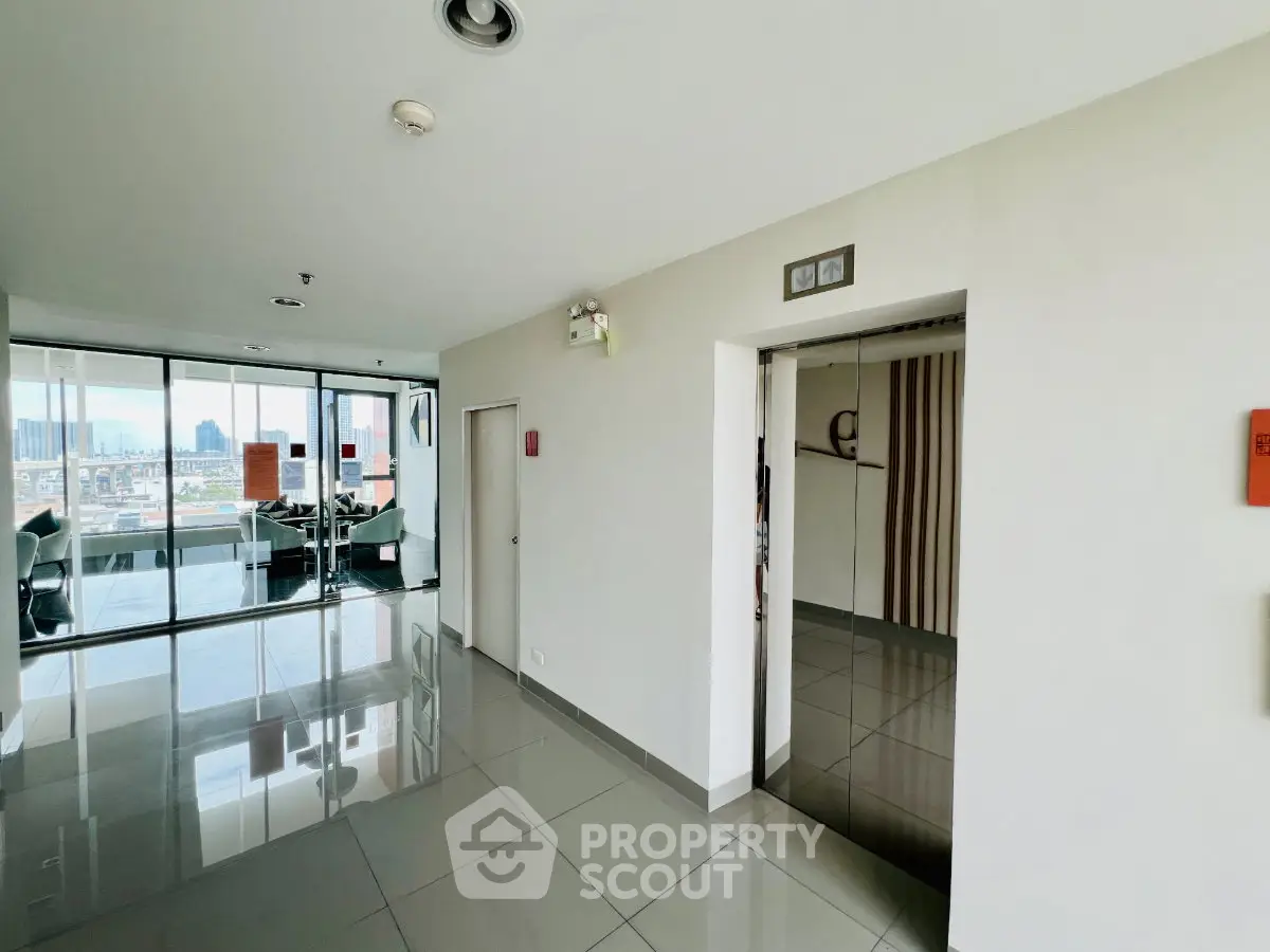 Modern building corridor with elevator and city view, showcasing sleek design and natural light.