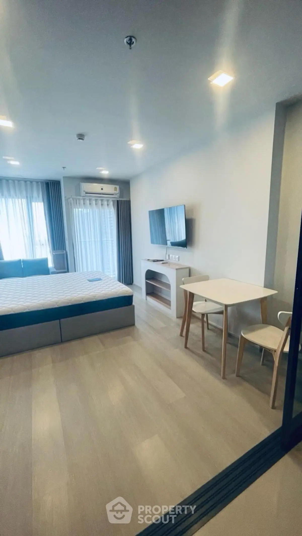 Modern bedroom with minimalist decor, featuring a cozy bed, wall-mounted TV, and a small dining area.