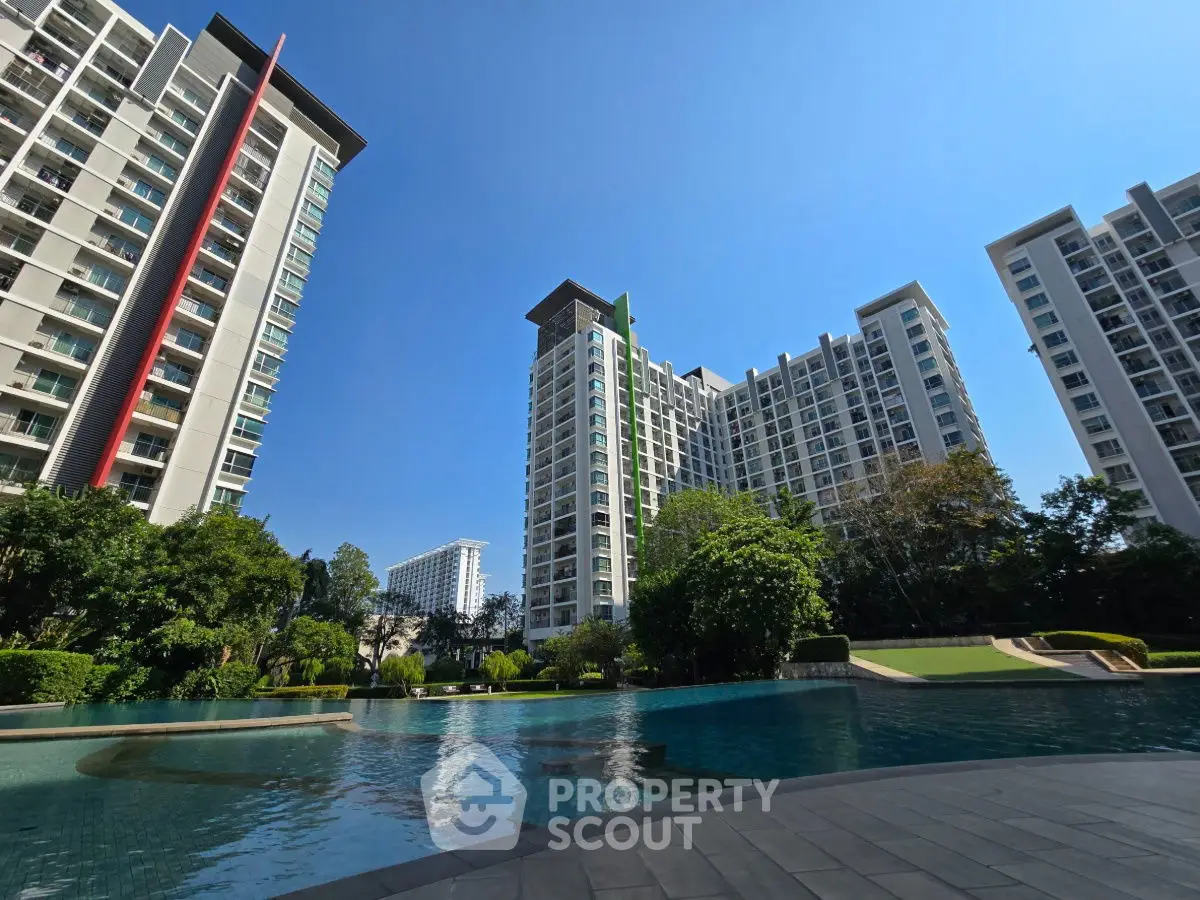 Luxurious high-rise condos with stunning pool and lush gardens under clear blue sky.