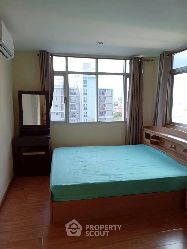 Cozy bedroom with large window offering city view, featuring a comfortable bed and wooden flooring.