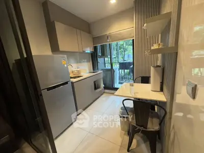 Modern kitchen with sleek cabinetry and dining area, featuring a view of the balcony and lush greenery.