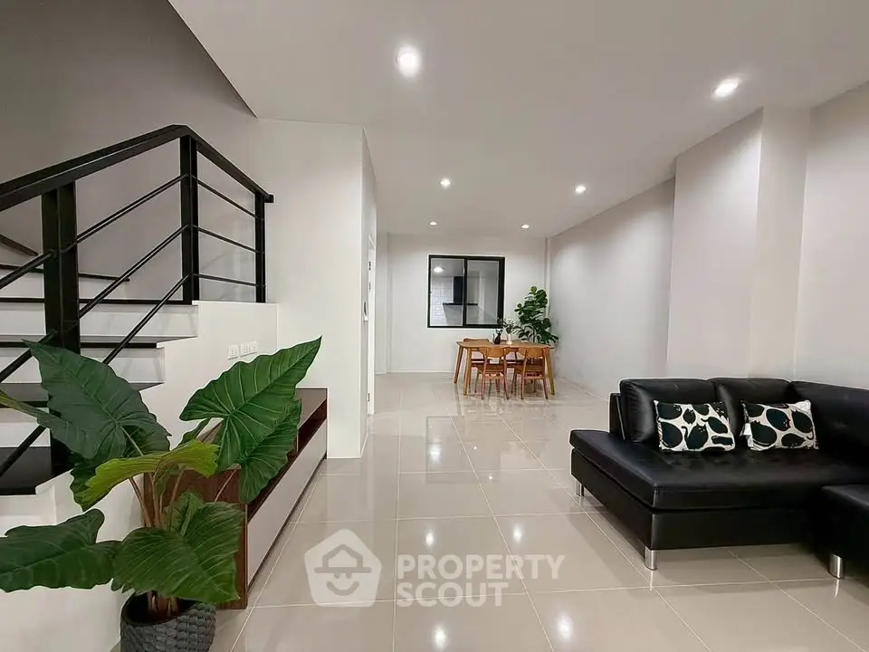 Spacious modern living room with sleek black sofa and elegant dining area, perfect for contemporary living.