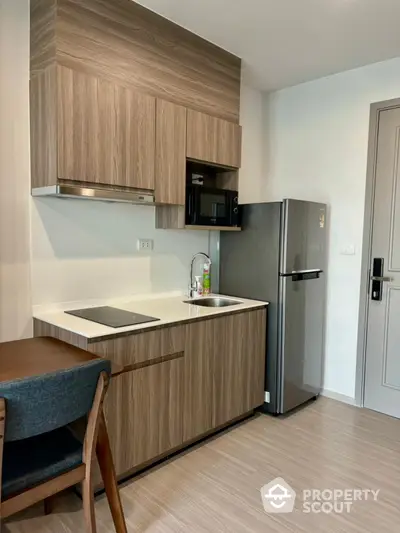 Modern compact kitchen with sleek wooden cabinetry and stainless steel fridge