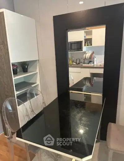Modern kitchen with sleek black countertop and transparent chairs, featuring open shelving and built-in microwave.