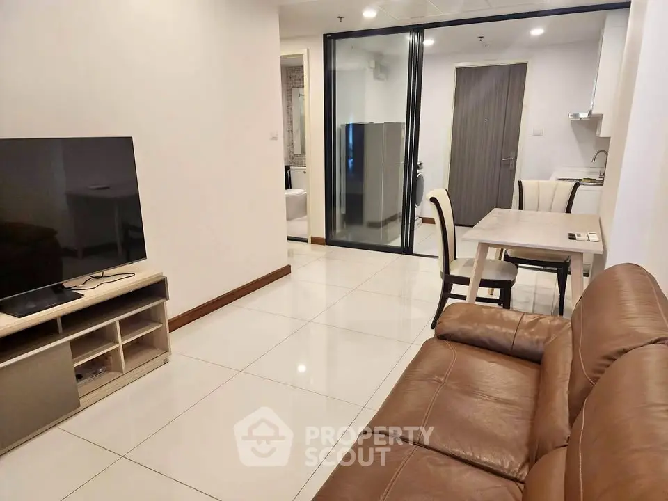 Modern living room with leather sofa and TV, open layout to dining area and kitchen.