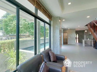 Spacious living area with large windows offering ample natural light, modern flooring, and a view of the lush outdoor greenery.