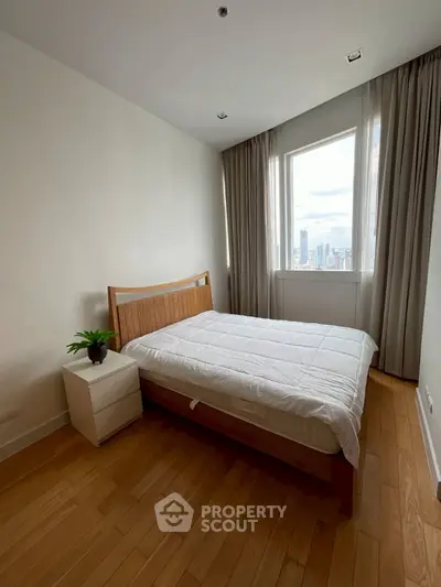 Cozy bedroom with wooden flooring and city view, featuring a comfortable bed and bedside table.
