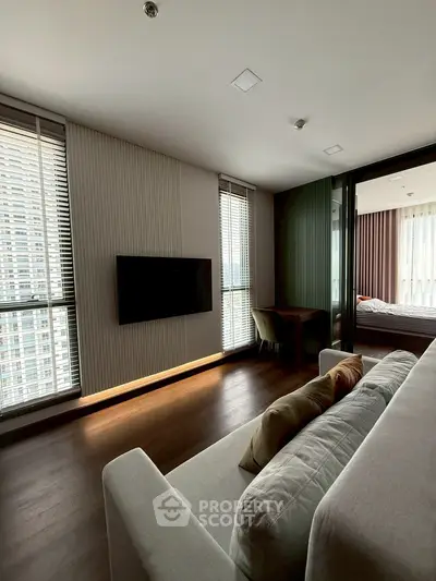 Modern living room with sleek design and large windows offering city views, adjacent to a cozy bedroom.