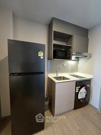 Modern compact kitchen with fridge, washing machine, and microwave in sleek design.