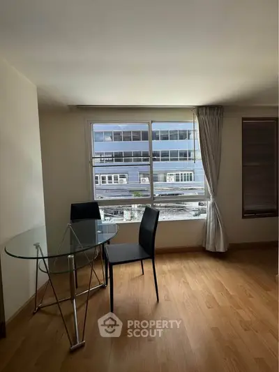 Bright living room with glass table and chairs, featuring large window with urban view.