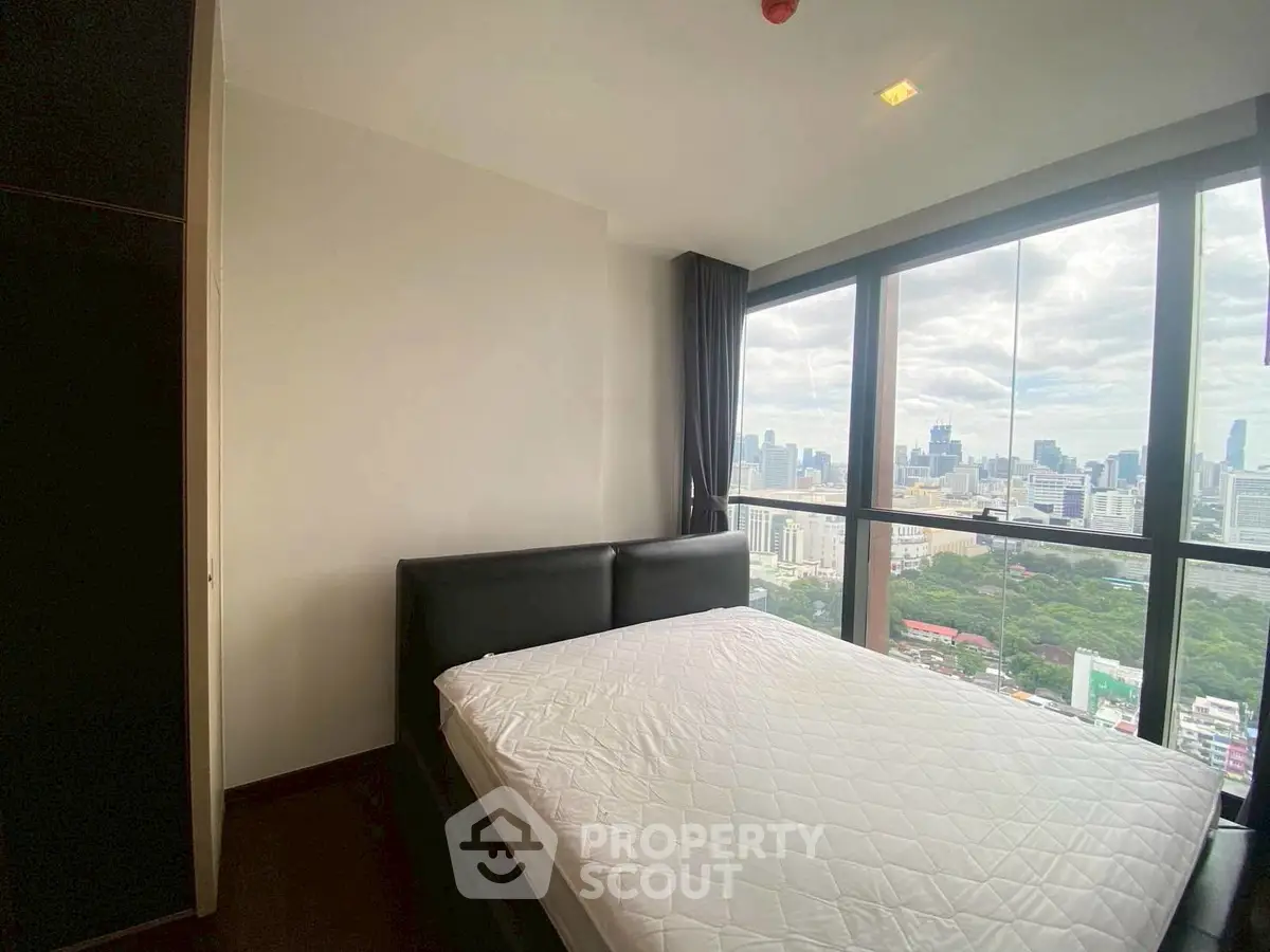 Modern bedroom with stunning city view from large windows in high-rise apartment.