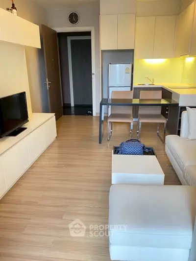 Modern open-plan living room with kitchen, featuring sleek furniture and wooden flooring.