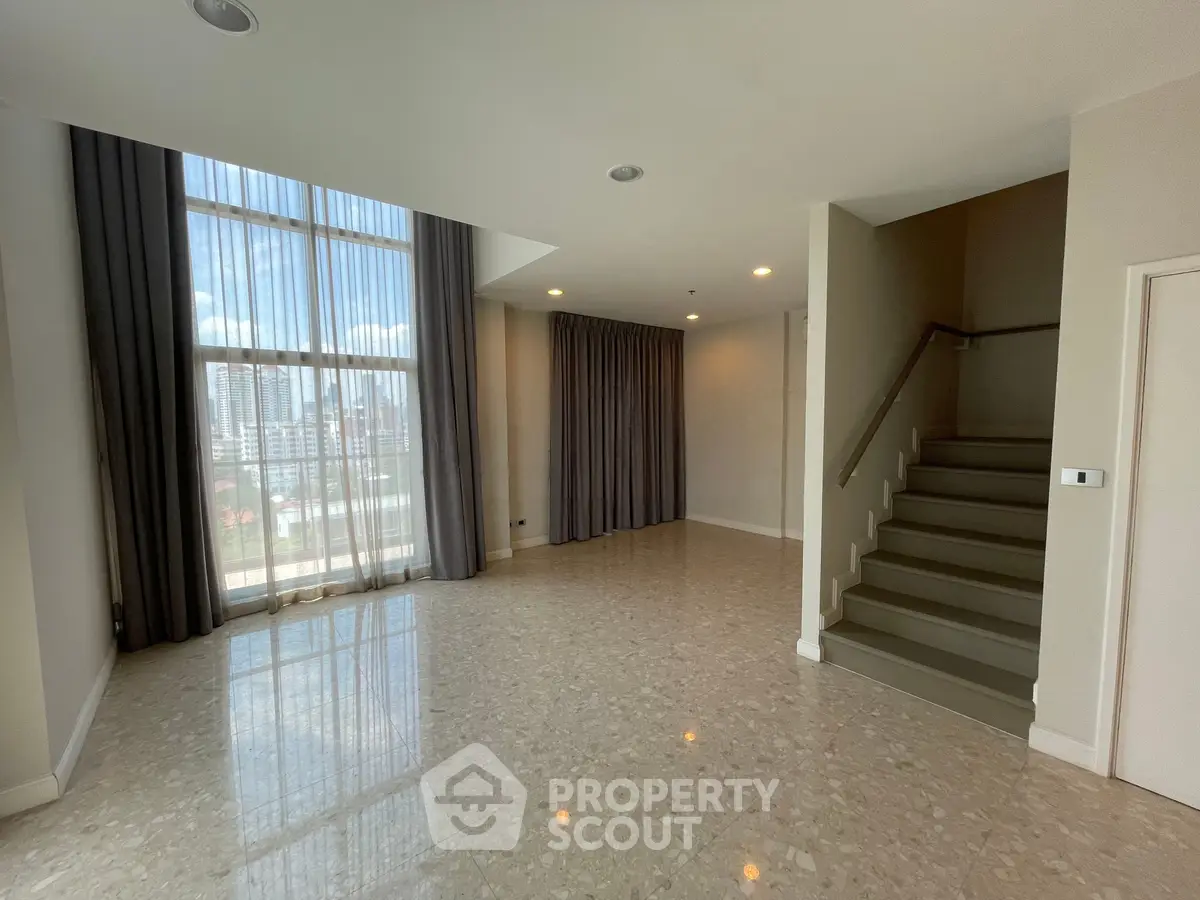 Spacious modern living room with high ceilings and large windows offering city views.