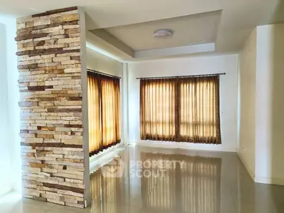 Spacious living room with stone accent wall and large windows with curtains, perfect for natural light.