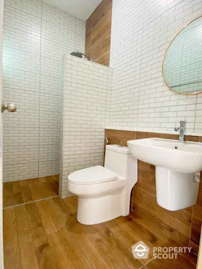 Modern bathroom with wood-style tiles, white brick walls, round mirror, and sleek fixtures.