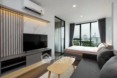 Modern studio apartment with stylish living area and city view, featuring sleek furniture and large windows.
