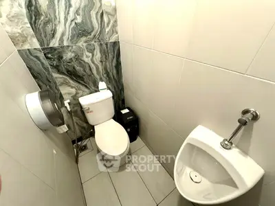 Compact modern bathroom with toilet and urinal, featuring stylish marble accent wall.