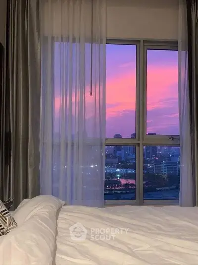 Stunning bedroom view with vibrant sunset over city skyline, perfect for urban living enthusiasts.