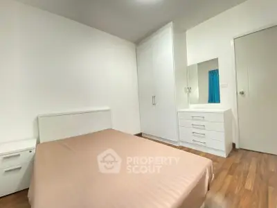 Modern minimalist bedroom with wooden flooring and white furniture.