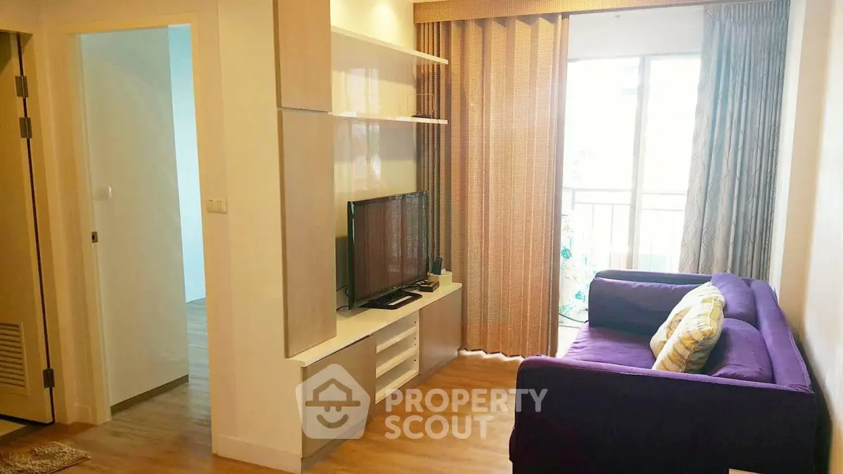 Cozy living room with purple sofa and natural light from balcony, perfect for relaxation.