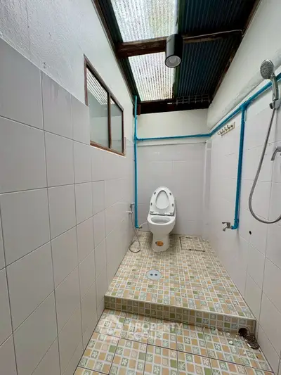 Compact bathroom with tiled walls and floor, featuring a toilet and shower area.