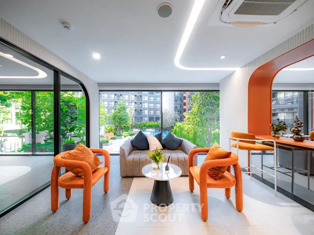 Modern living room with vibrant orange chairs and large windows overlooking lush greenery.