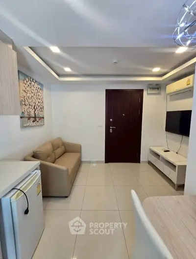 Modern living room with sleek design, featuring a cozy sofa, wall-mounted TV, and compact fridge.