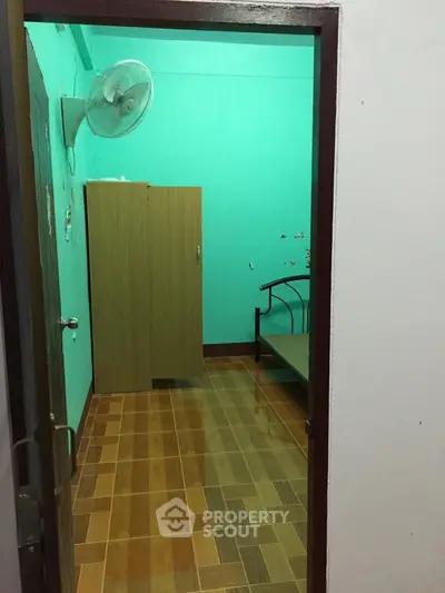 Compact bedroom with wooden wardrobe and bed, featuring a wall-mounted fan and tiled flooring.