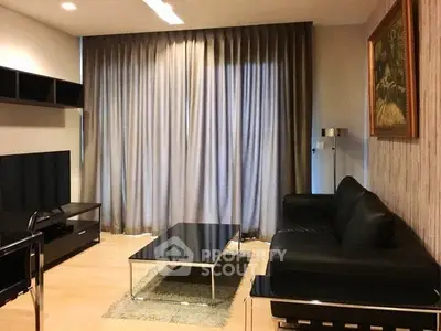 Modern living room with sleek black furniture and floor-to-ceiling curtains.
