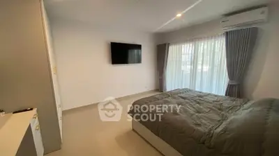 Modern bedroom with large window and wall-mounted TV, featuring sleek design and natural light.