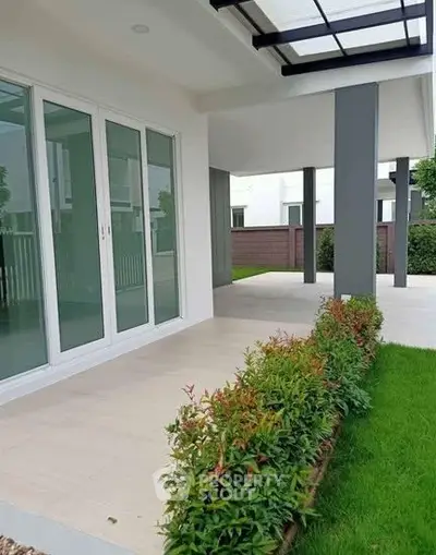 Modern home exterior with sleek design and lush garden, featuring large glass doors and covered patio.