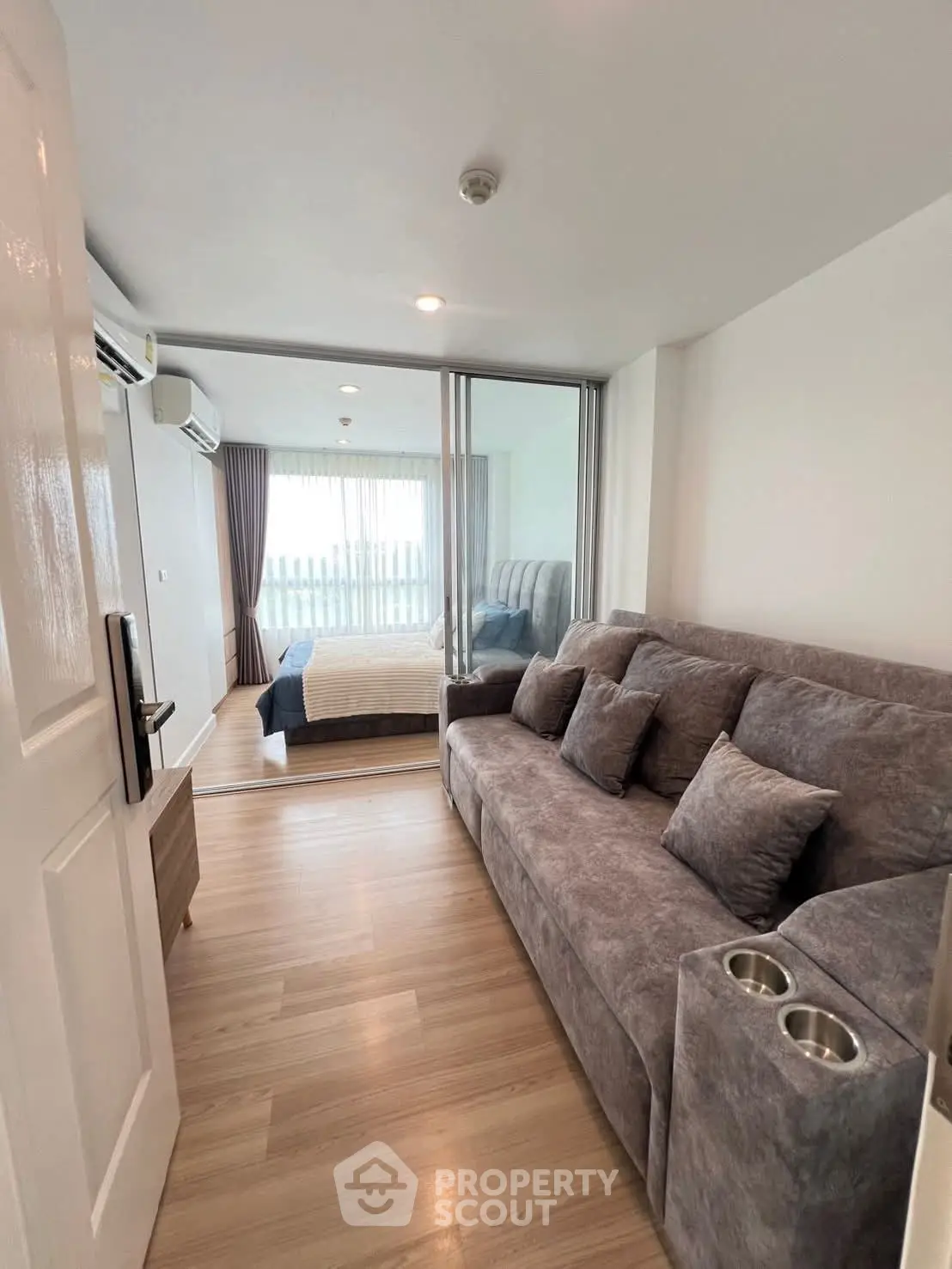 Modern apartment with cozy living room and bedroom, featuring stylish gray sofa and wooden flooring.