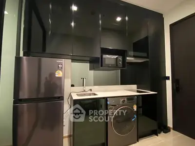 Modern kitchen with sleek black cabinets, fridge, and washing machine.