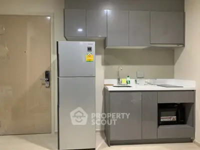 Modern compact kitchen with sleek cabinetry and stainless steel fridge in a stylish apartment.