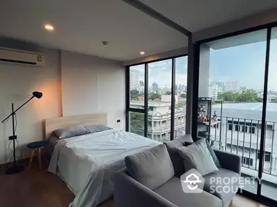 Spacious bedroom with modern design, featuring a comfortable bed, cozy sitting area, and floor-to-ceiling windows offering an urban view.