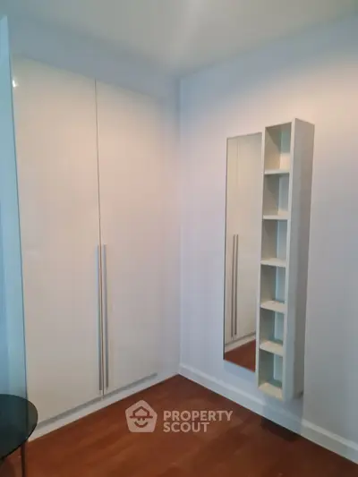 Modern bedroom with sleek wardrobe and wall-mounted shelves, featuring elegant wooden flooring.