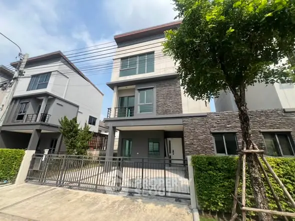 Modern three-story house with stone facade and gated driveway in suburban neighborhood.