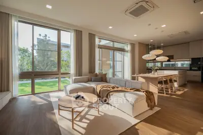 Spacious modern living room with open kitchen and large windows overlooking a garden.