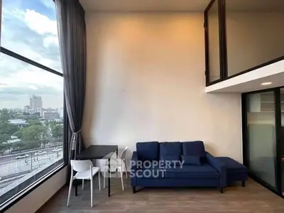 Modern living room with large window and city view, featuring a blue sofa and dining table.